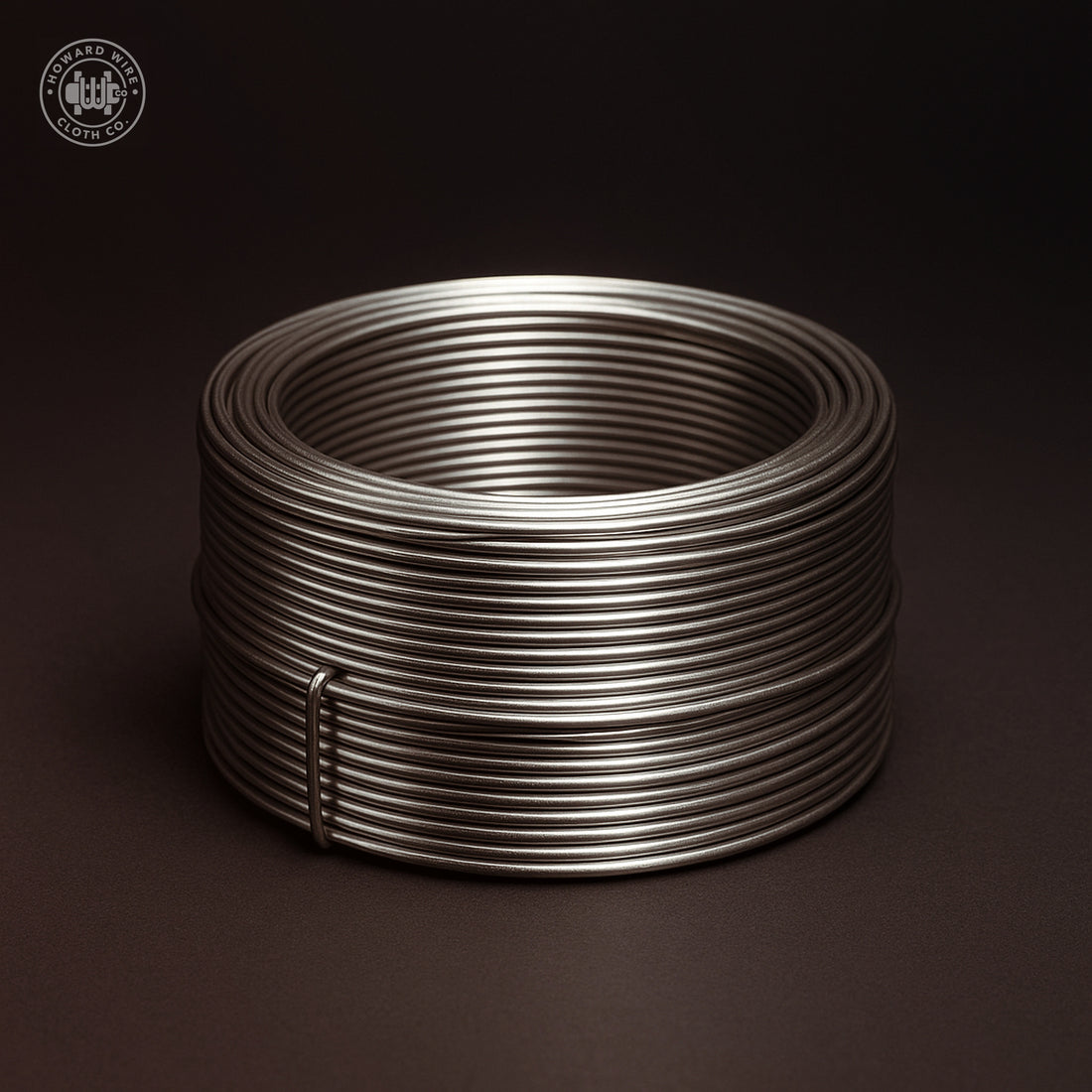 Studio photograph of a coil of .025 inch diameter type 304 stainless steel wire on a dark graphite background.